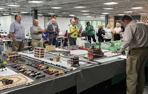 Several people standing around a scale model diorama of a mix of swine-related facilities