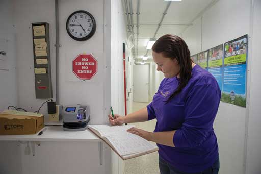 A person with wet hair signs a log book near a time clock